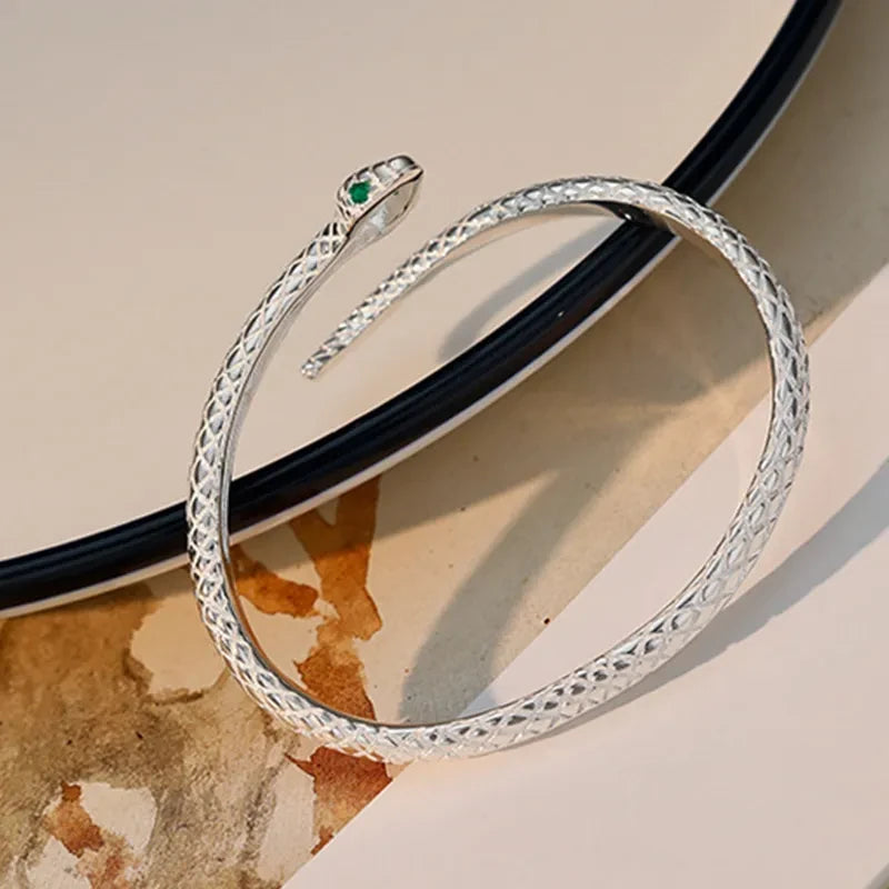 Silver-tone serpent cuff with green eye accents on a warm stone surface