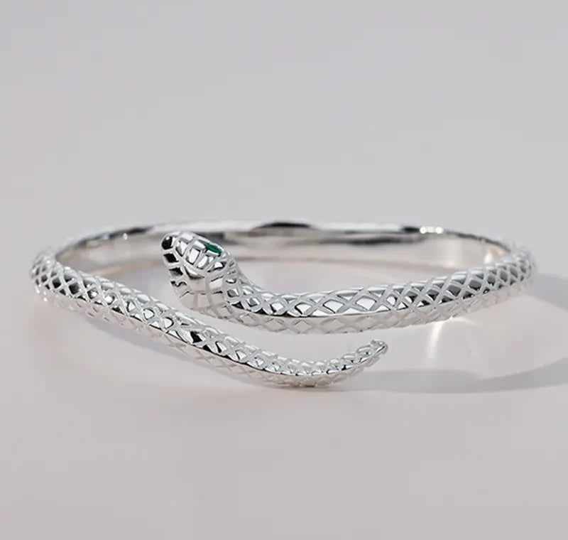 Silver-tone serpent bracelet resting on a pale surface with the open ends visible