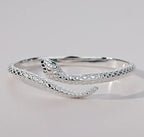 Silver-tone serpent bracelet resting on a pale surface with the open ends visible