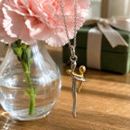 Hug pendant necklace displayed beside flowers