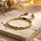 Copper and brass bead bracelet with an adjustable braided cord on a pale stone surface
